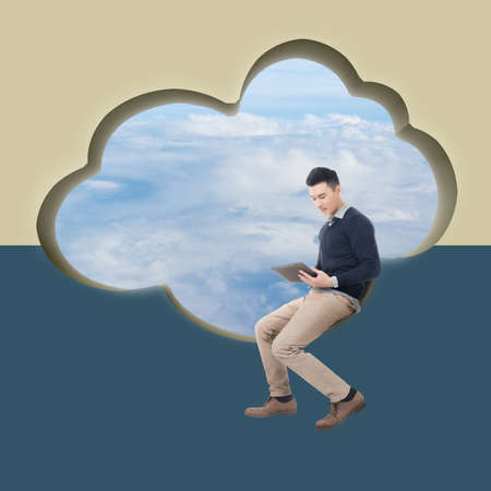 Cloud concept with man sit at a cloud shaped wall and using tablet.の写真素材