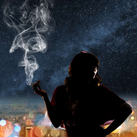 Silhouette of Asian christmas girl holding a cigar in the city night.の写真素材