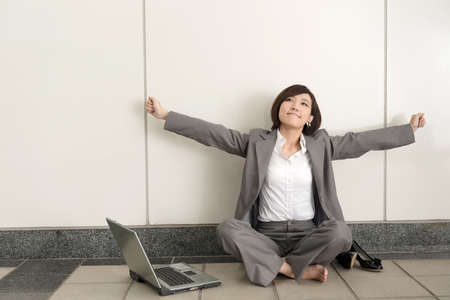 Asian young business woman take off her shoes and relax sitting on ground in modern building.の写真素材