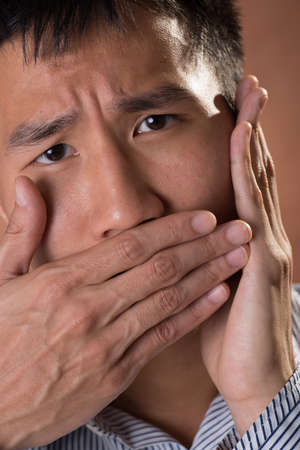 Young Chinese frank businessman closed his mouth by hand, closeup portrait in studio.