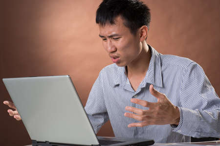 Angry business man of Chinese sitting on chair and looking at laptop on desk in studio.