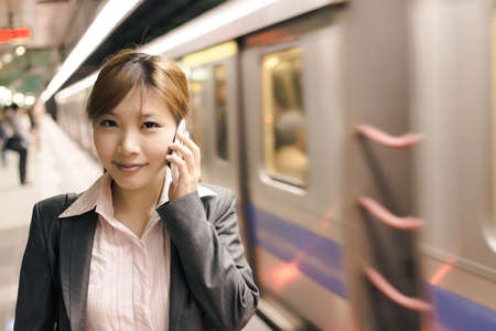Asian young business woman use cellphone in the MRT station, shot at Xinyi business district, Taipei, Taiwan.の写真素材