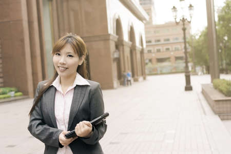 Attractive young business woman hold a laptop and look at you, shot at Xinyi business district, Taipei, Taiwan.の写真素材