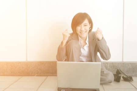 Cheerful business woman sitting and using laptop on ground.の写真素材