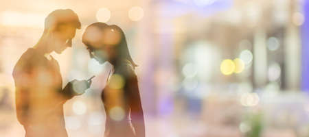 Couple using cellphone, silhouette portrait.の写真素材
