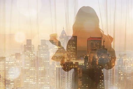 Silhouette of a woman standing in front of a window and holding a cup of coffee.の写真素材