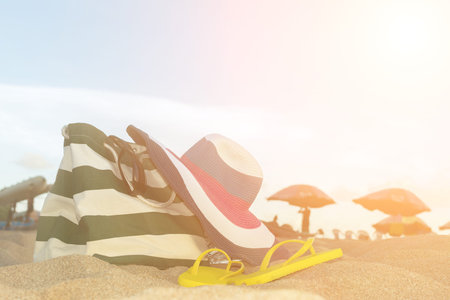 Summer concept of straw hat, bag, sunglasses and flip flops on a tropical beach.の写真素材