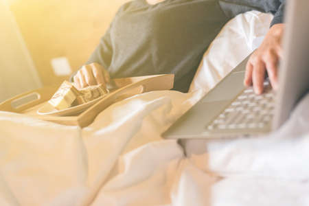 concept of working at home with woman using laptop on bedの写真素材
