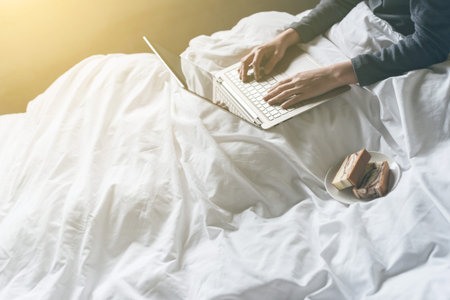 concept of working at home with woman using laptop on bed