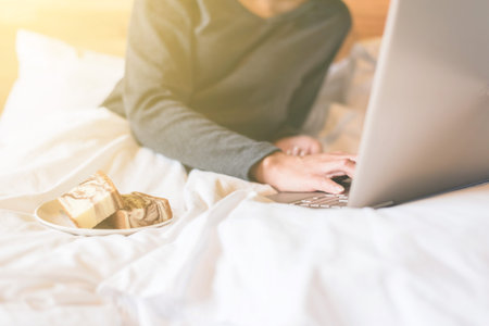 concept of working at home with woman using laptop on bedの写真素材