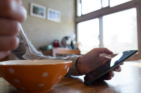 woman eat cereal with milk when using smartphoneの写真素材