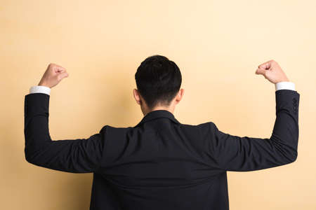 young Asian business man show you his muscle, rear view closeup portrait on studio yellow backgroundの写真素材