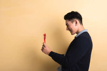 Chinese young man hold red envelope in the new year in studio yellow backgroundの写真素材