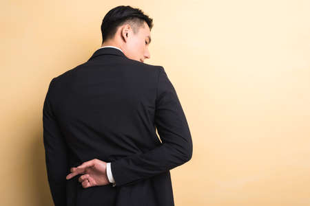 young Asian business man give you a gesture of fake, closeup portrait on studio yellow backgroundの写真素材