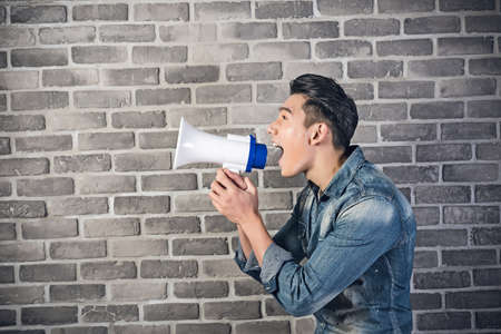 Asian young man hold a bullhorn against the gray brick wallの写真素材