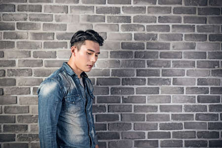 sad Asian young man portrait against the gray brick wallのeditorial素材