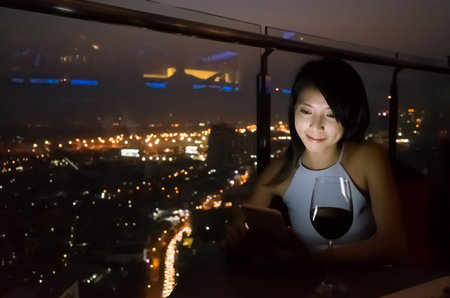 asian lady read message on mobiel at luxury restaurant in the night, bangkok, asiaの写真素材