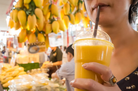 asian woman hold a mango juice in the market at bangkok, asiaの写真素材