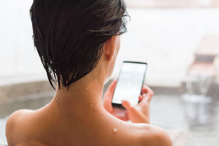 rear view of asian mature woman using cellphone at the hot spring poolの写真素材