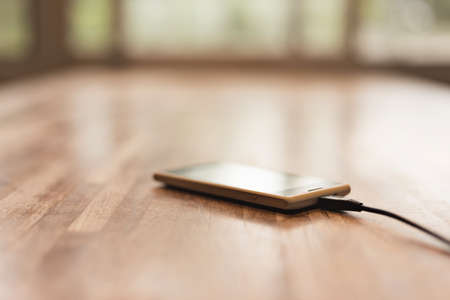 Mobile smart phone charging on wooden deskの写真素材