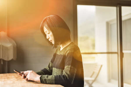 Asian woman using cellphone in the houseの写真素材