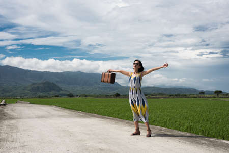 Asian woman traveling and raising her hand at countrysideの写真素材