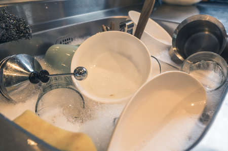dirty dishes in the kitchen sink with water at homeの写真素材