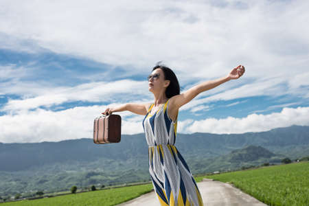 Asian woman traveling and raising her hand at countrysideの写真素材