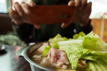 woman take a picture on hot pot with vegetables and porkの写真素材