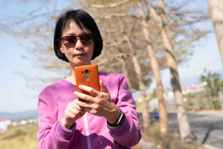 mature Asian woman using the smart phone at outdoorの写真素材