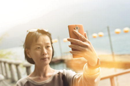 traveling mature Asian woman selfie by mobile phone at Sun Moon Lake, Taiwan