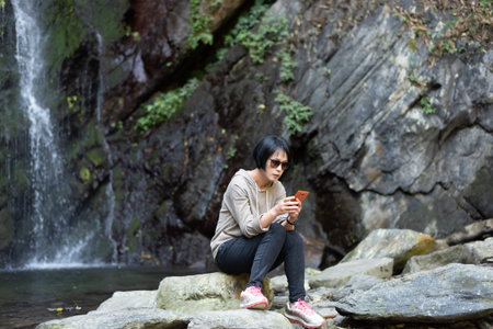 Asian woman using mobile phone near the waterfall at outdoor