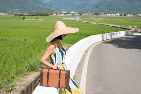 woman wait and hold a suitcase on the way at countryside