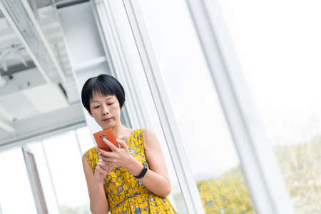 mature Asian woman using cellphone at a modern buildingの写真素材