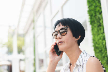 Asian woman sit and talk on cellphone in the outdoorの写真素材