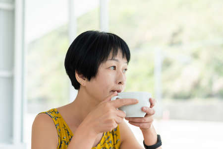 mature Asian woman hold a cup of coffee in a shopの写真素材