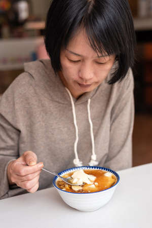Asian woman eat tofu pudding at a storeの写真素材