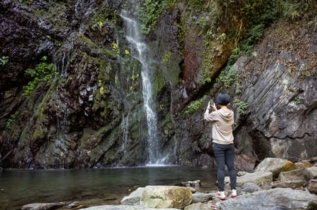Asian woman take a picture near the waterfallの写真素材
