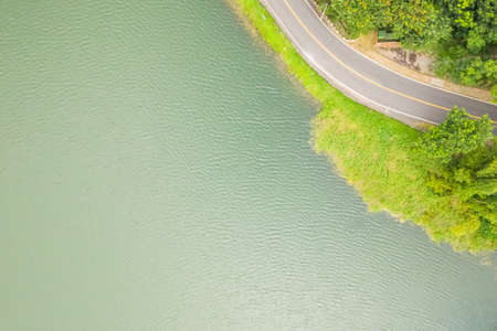 road under forest near a lake, aerial view in the daytimeの写真素材