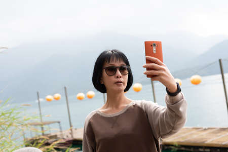 traveling mature Asian woman selfie by mobile phone at Sun Moon Lake, Taiwanの写真素材