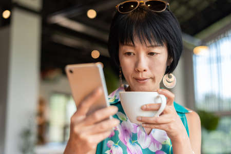 woman holding a cup of coffee and check text in a mobile in the shopの写真素材