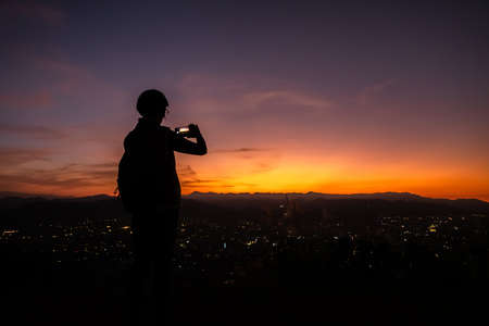 silhouette of traveling woman take a photo by smartphone at the top of a hill in cityの写真素材