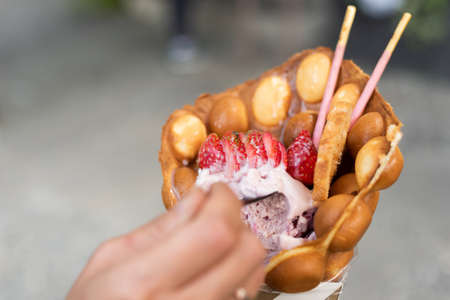 woman eat a waffle ice cream with strawberries at a streetの写真素材