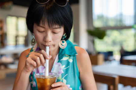 mature Asian woman holding a cup of ice tea in a restaurantの写真素材