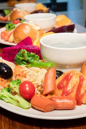 Delicious and abundant breakfast with bread, pasta, mandarin oranges, passion fruit, dragon fruit, grapes, and purple rice soy milk in the plate.の写真素材
