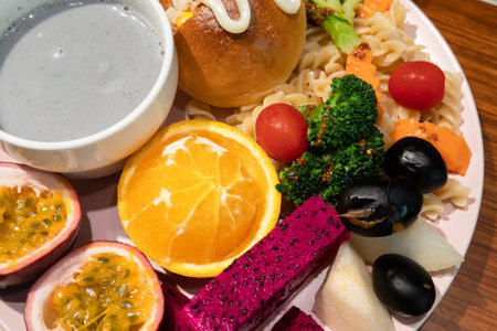 Delicious and abundant breakfast with bread, pasta, mandarin oranges, passion fruit, dragon fruit, grapes, and purple rice soy milk in the plate.の写真素材