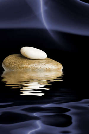 Zen stones on black background with blue smoke reflected in waterの写真素材