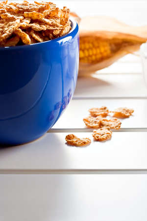 Cornflakes in a blue bowl on white wooden table with a cobの写真素材