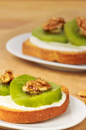 Toast with kiwi, cheese and walnuts on a piece of sackcloth with walnuts around.の写真素材