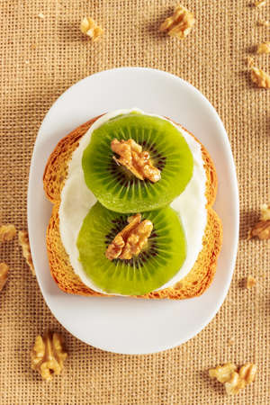 Toast with kiwi, cheese and walnuts on a piece of sackcloth with walnuts around. View from aboveの写真素材